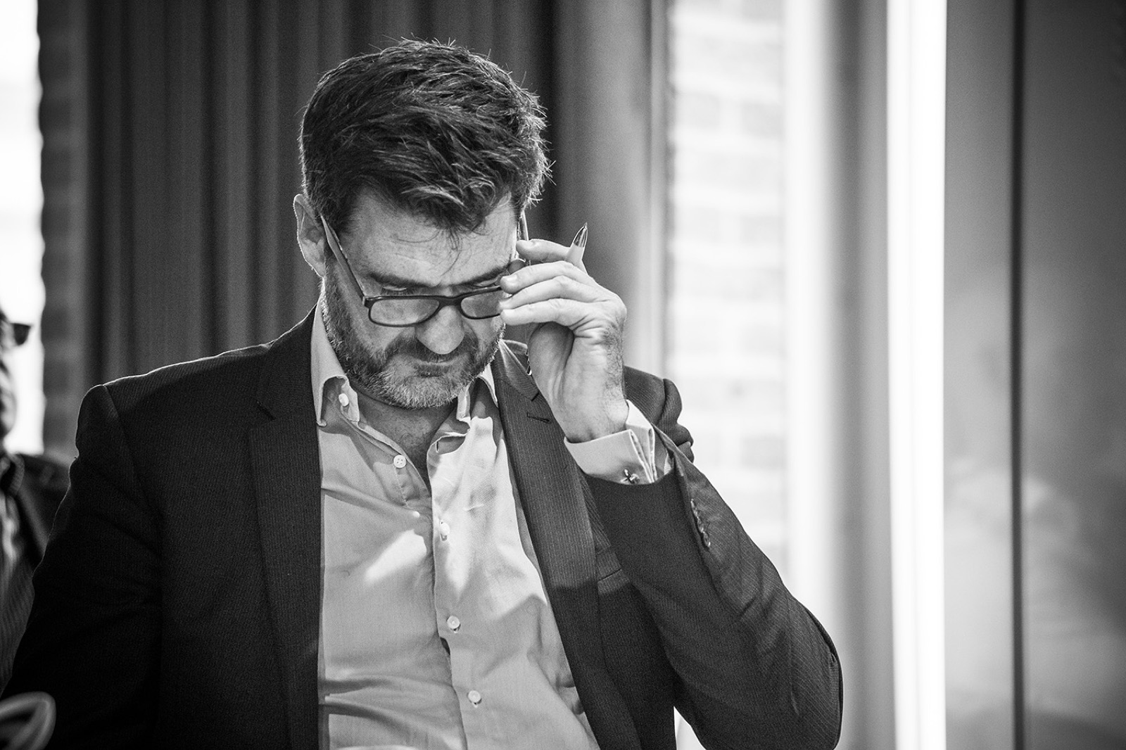 Tony Wood looking down while adjusting his glasses in a black-and-white conference photo.