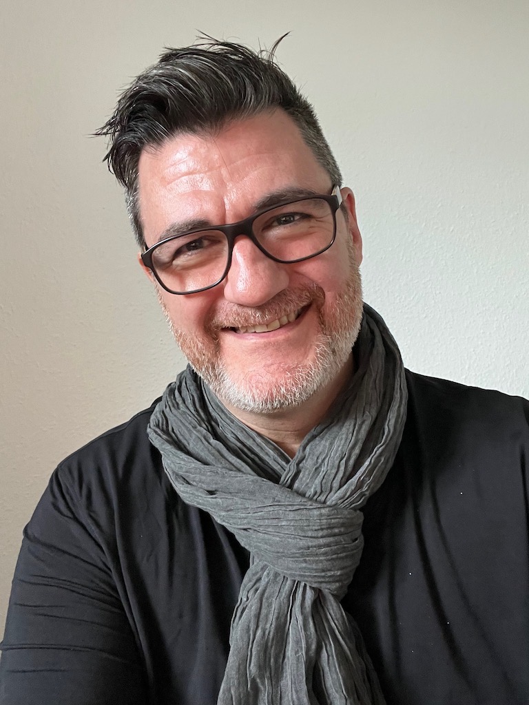 Tony Wood wearing glasses and a grey scarf.