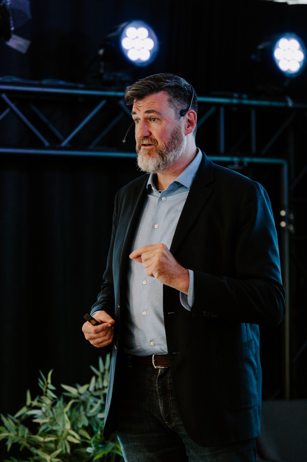 Tony Wood speaking on stage with a headset microphone.