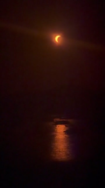 A distant crescent Sun above the sea with warm light reflected on the water.