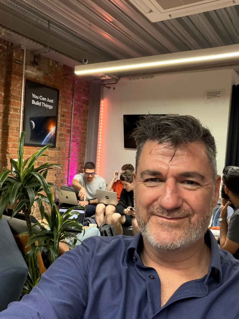 Tony Wood at the OpenAI Build Week Community Builders Lounge in London, with other builders working behind him.
